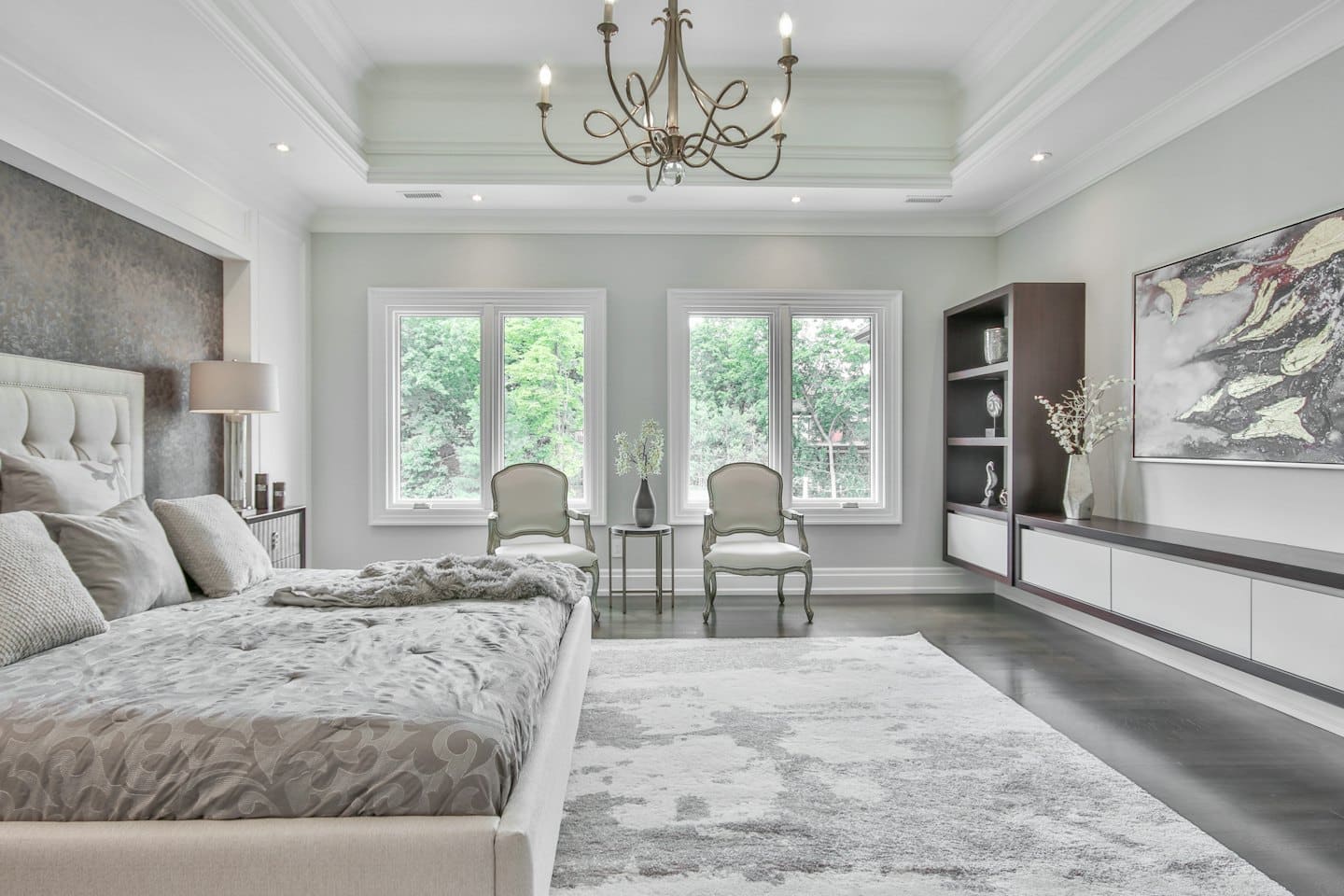 Luxurious master bedroom with king bed and view of trees.